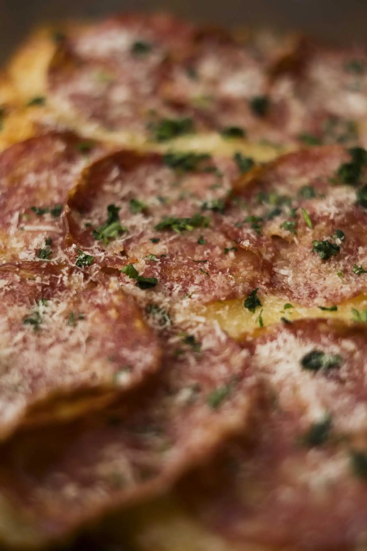 Közelkép szalámis pizzáról, sajttal és friss zöld fűszerrel megszórva, aranybarnára sütött tésztán.