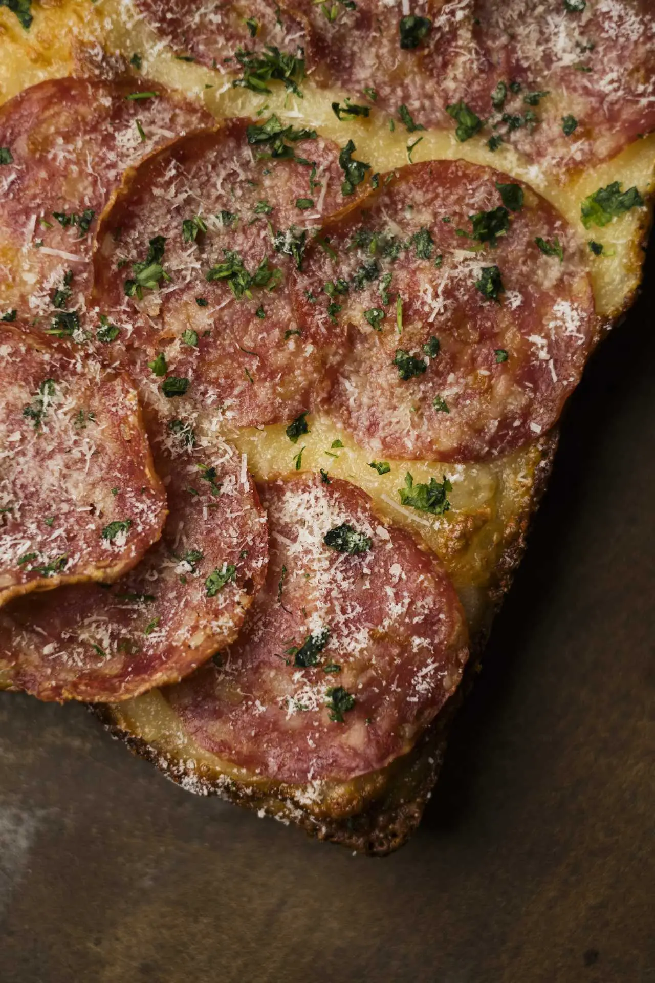 Szalámis pizzaszelet közelről, sajttal és friss zöld fűszerrel megszórva, aranybarnára sült, ropogós szélekkel.