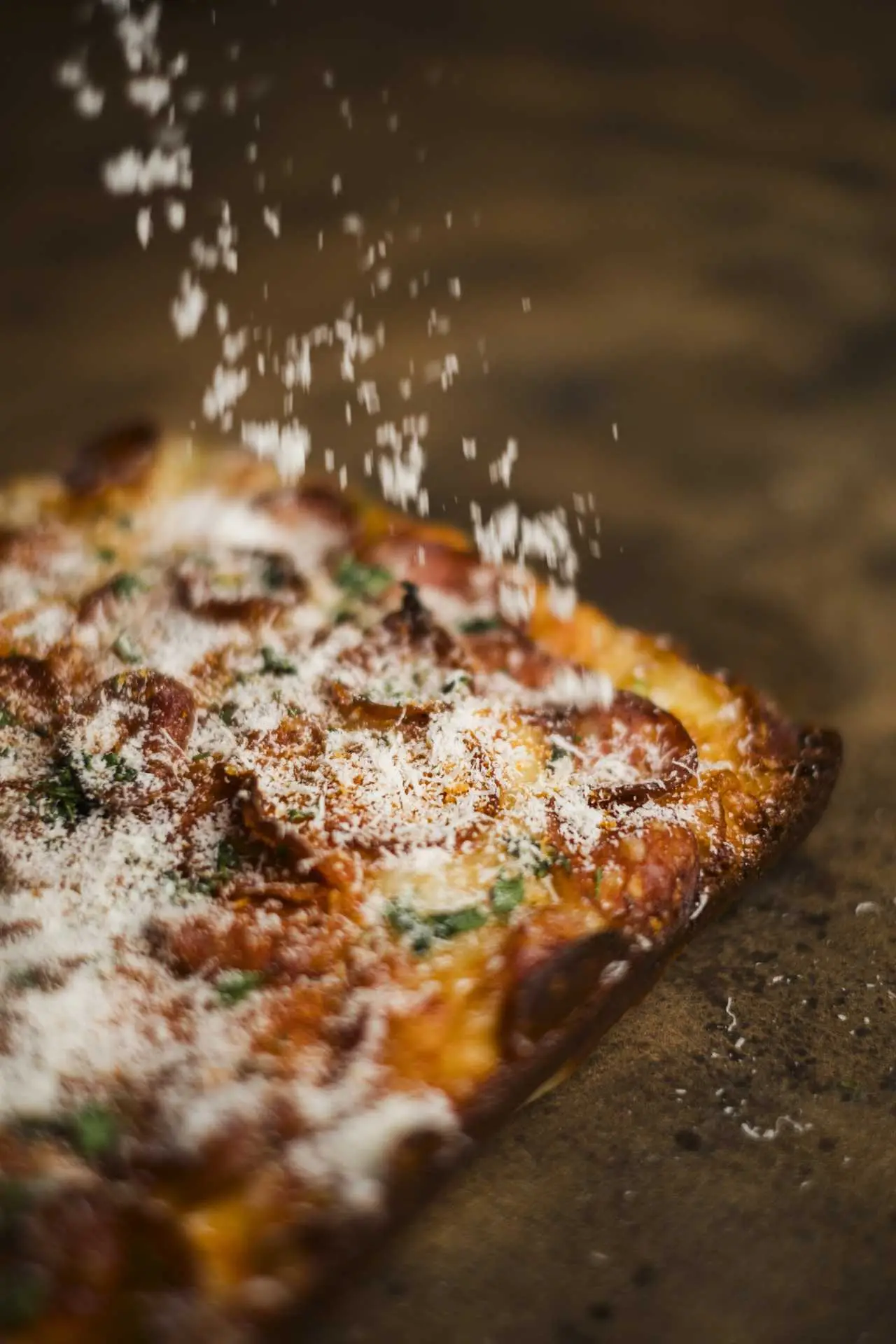 Frissen sült pizzára hulló reszelt sajt közelről, ropogós tésztán, zöld fűszerrel megszórva.