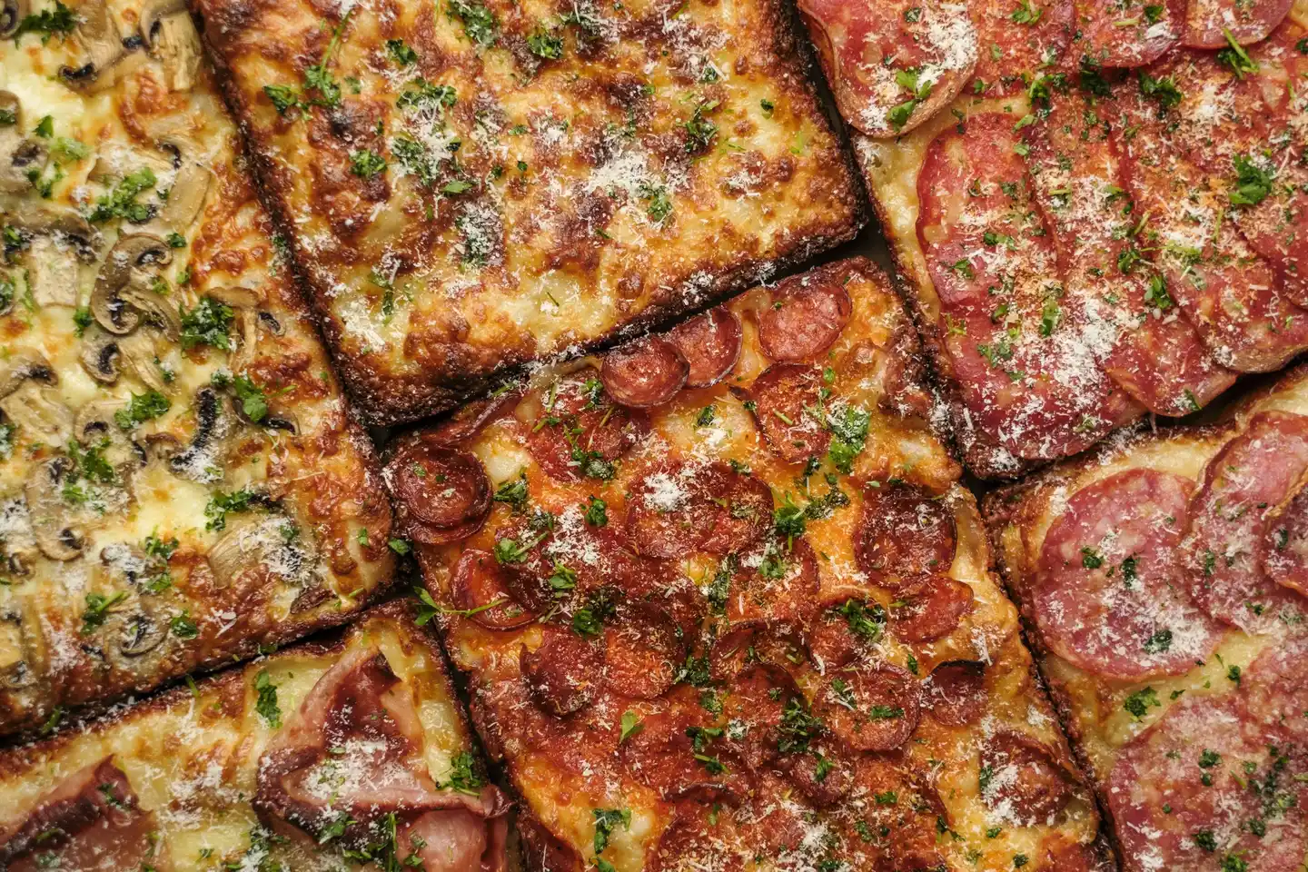 Sajtos, kolbászos, szalámis és gombás pizzák közelről, friss zöld fűszerrel megszórva.